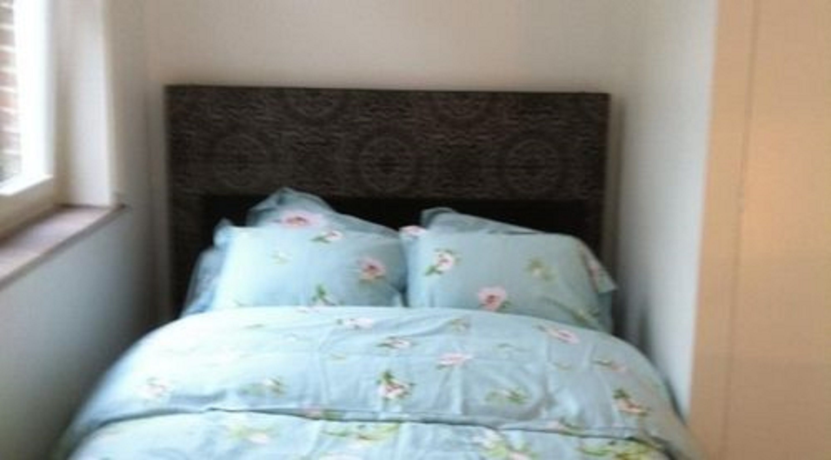A small bedroom with a bed, a window, and a dark headboard.
