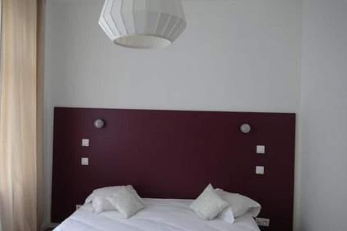 A hotel room with a bed, a headboard with control buttons, and a hanging light fixture.