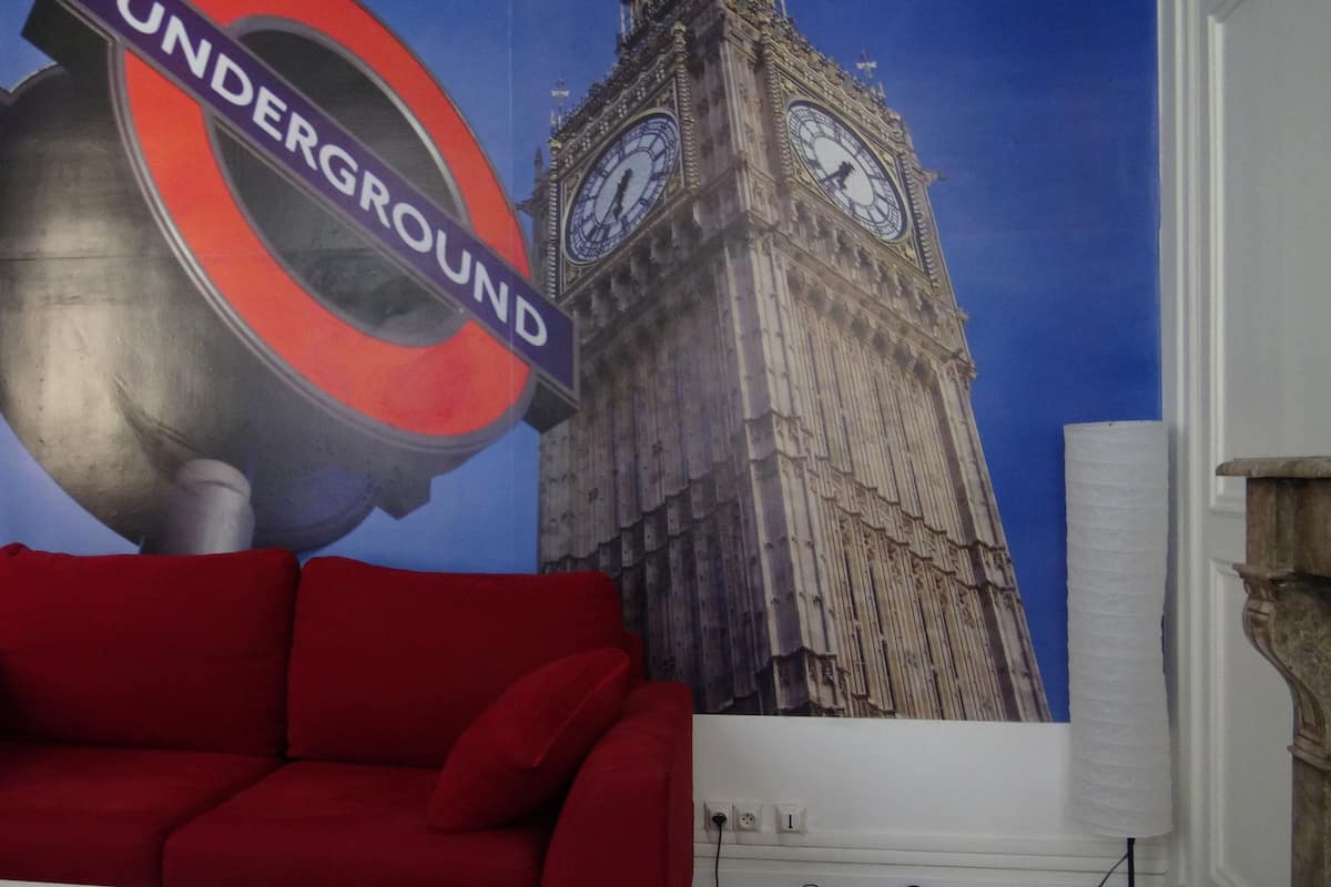 A room with a red sofa, a wall mural of the London Underground sign and Big Ben, and a white wall with a power outlet.