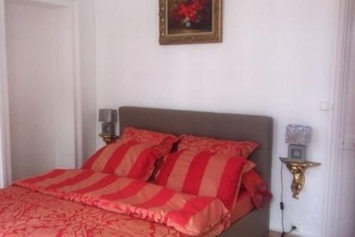 A bedroom with a bed, pillows, a nightstand, and a wall-mounted lamp.