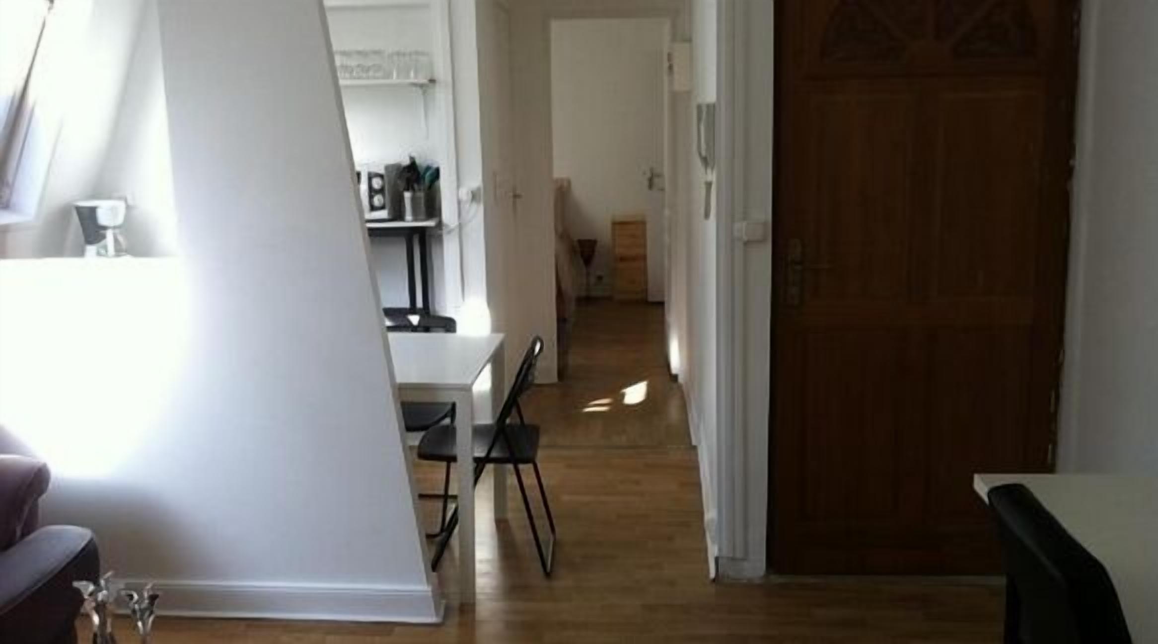 A hallway with a wooden floor leading to a door. There is a dining area with a table and chairs on the left.