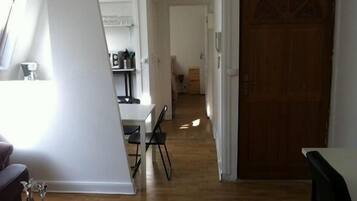 A hallway with a wooden floor leading to a door. There is a dining area with a table and chairs on the left.