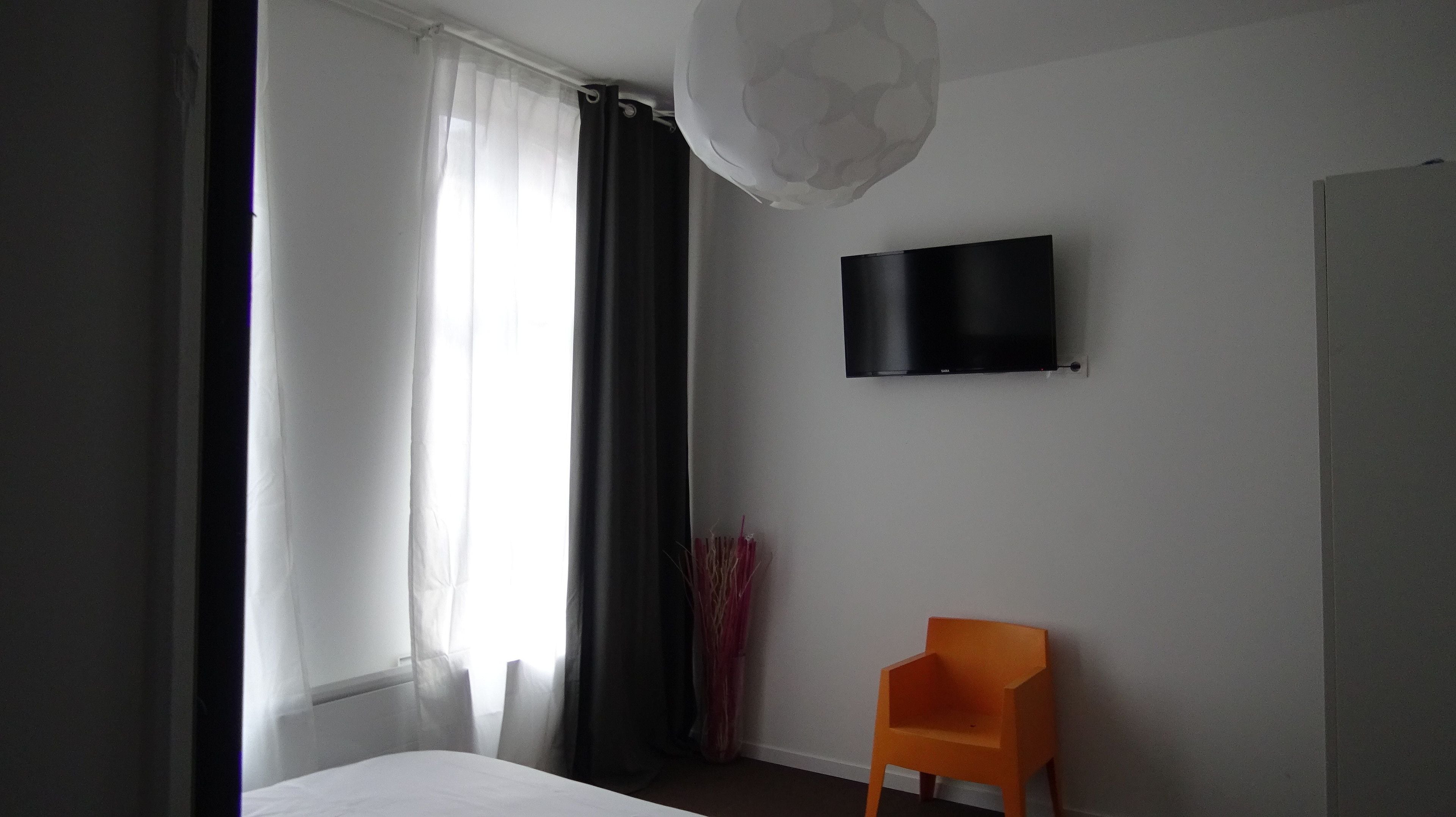 A hotel room with a bed, a TV mounted on the wall, and a chair.
