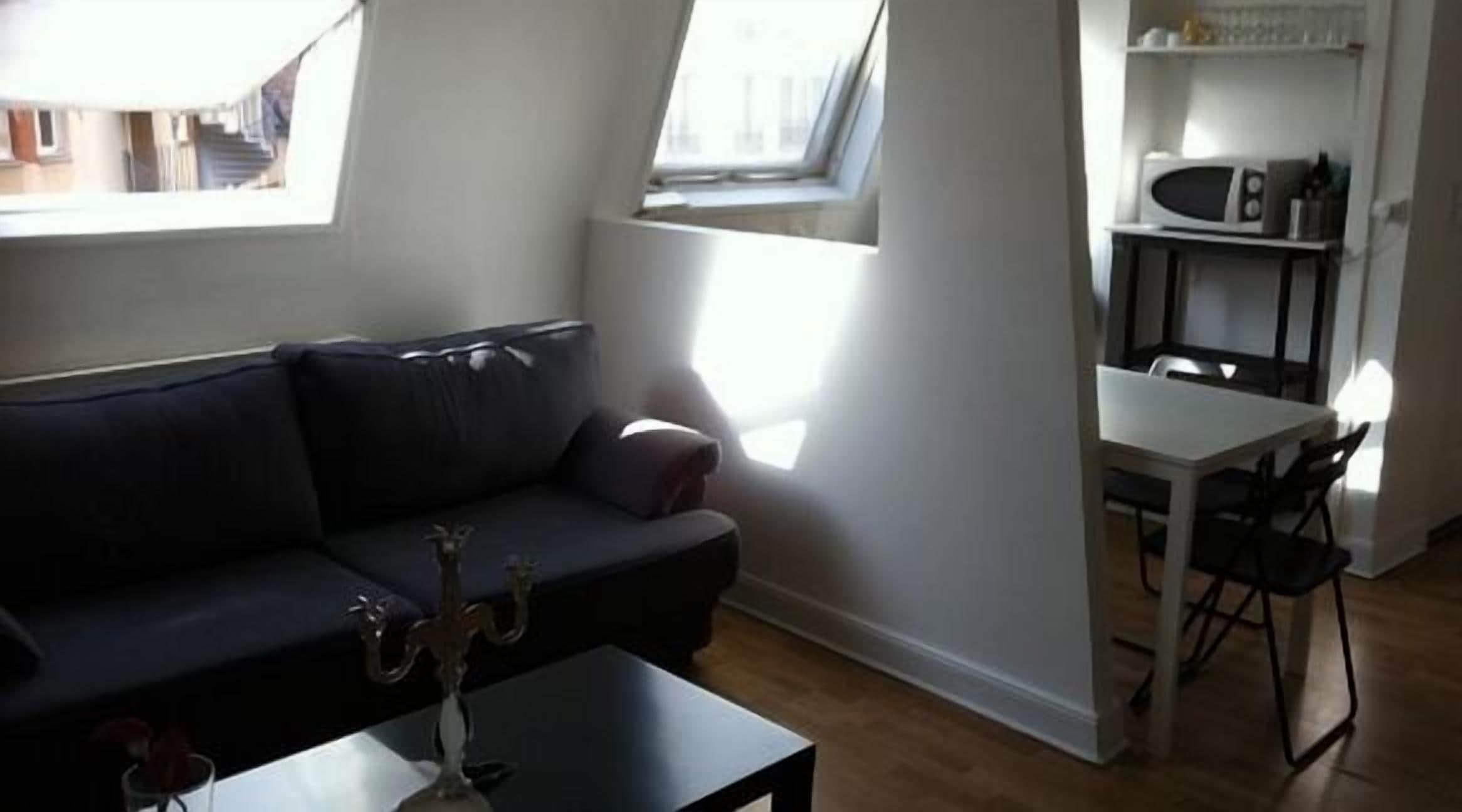 A modern living room with a dark sofa, a small table with a candle, and a dining area with a white table and chairs.
