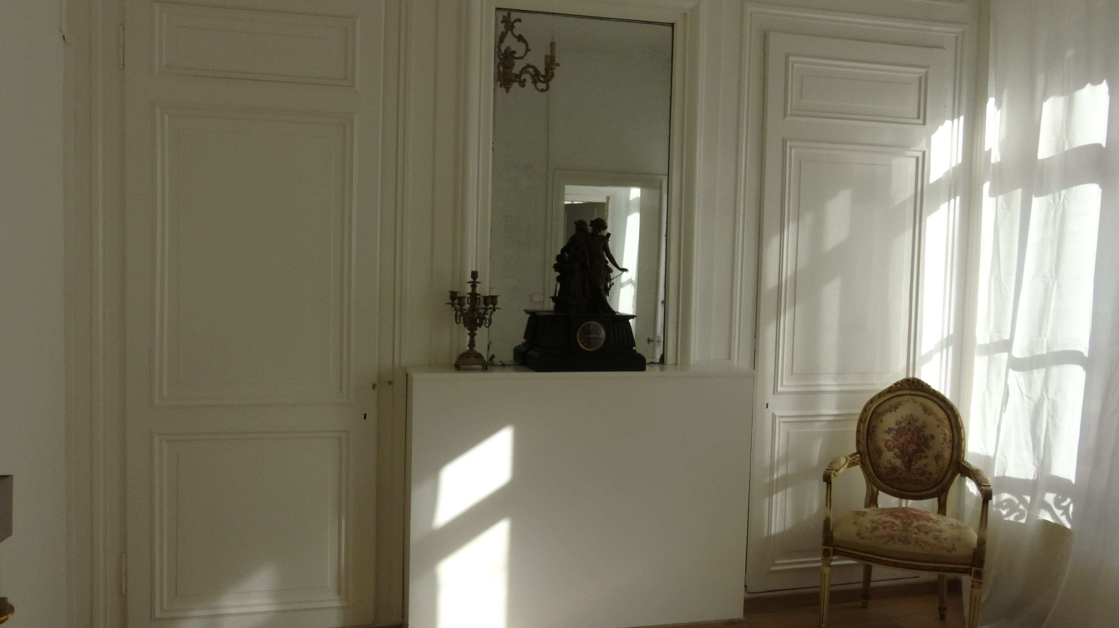 A room with a large mirror, a statue, a candelabra, and a chair.