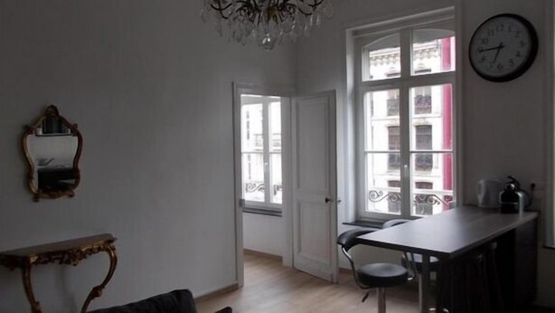 A room with a dining table, chairs, a chandelier, a mirror, and a view through a window. - Nationale AppartHotel (Lille)