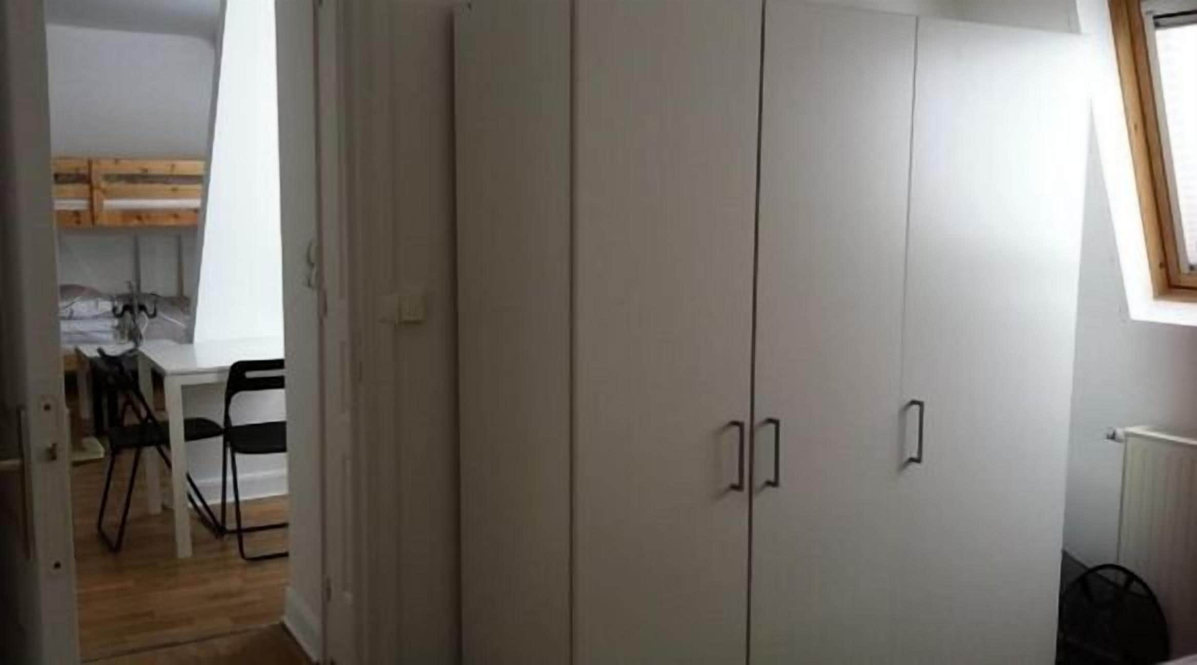 Una habitación con un armario grande, una mesa de comedor con sillas y un radiador.
