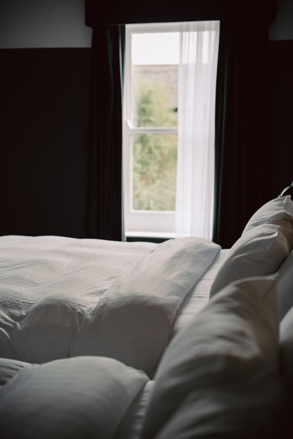 Una cama con ropa de cama blanca en una habitación con ventana.