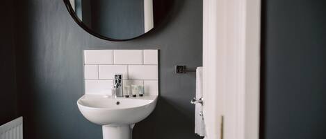 A bathroom with a white sink, a round mirror, and a towel rack.