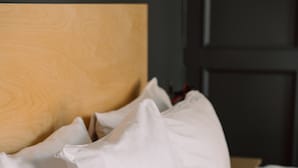 Una cama bien tendida con ropa blanca y almohadas, cabecera de madera y mesita de noche de madera.