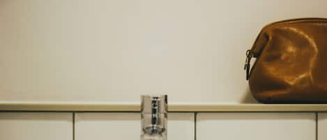 Un baño con pared de azulejos blancos, grifo cromado y bolso de cuero marrón en la pared.