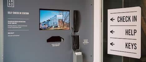 Een zelf incheckpunt met een scherm waarop een incheckmelding staat, een telefoon en borden met pijlen voor inchecken, hulp en sleutels.