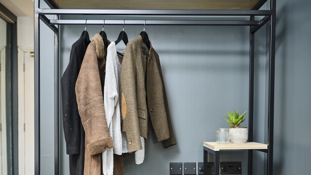 Un armario metálico con varios estantes, una zona para colgar ropa y una mesita con una planta.
