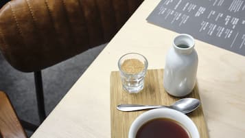 Una mesa de madera con un menú, un azucarero, una jarra blanca, una cuchara y una taza de té.