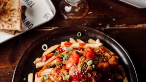 Una mesa de comedor con diversos alimentos, incluyendo un vaso de bebida helada con una rodaja de naranja, un plato de papas fritas y un plato con pollo y verduras.