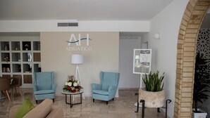 A modern lobby with two blue armchairs, a beige sofa, a small table with a lamp, and a wall-mounted display. - Hotel Adriatico (Tricase)