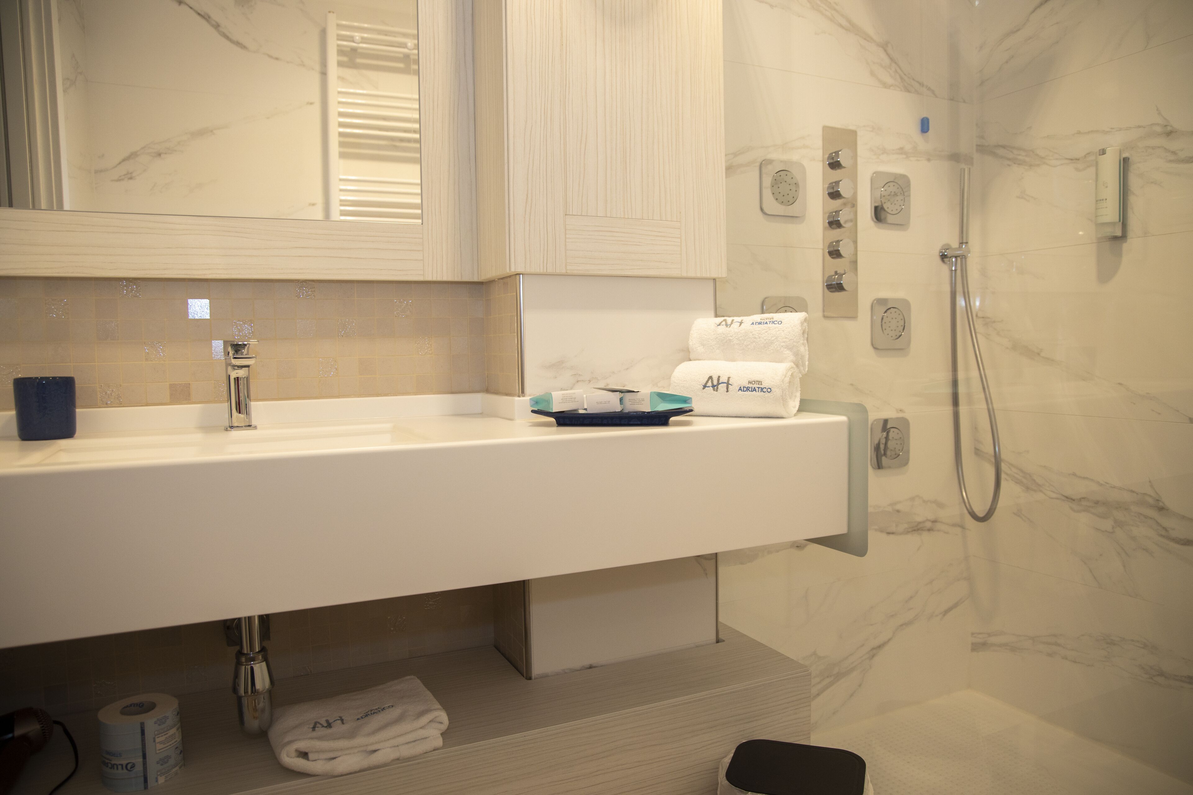 A modern bathroom with a marble sink, towel dispenser, and a handheld showerhead.