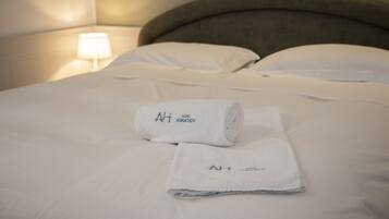 A neatly made bed with white linens and two rolled towels with "AH HOTEL ADRIATICO" text.