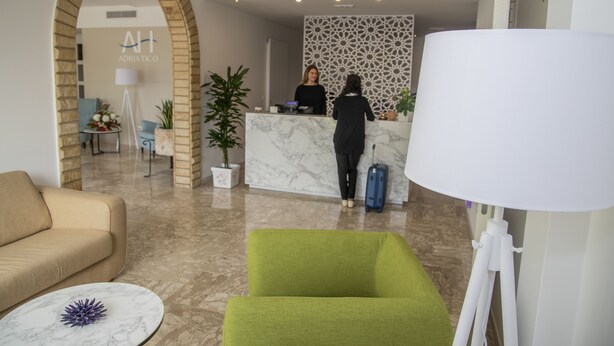 A reception area with a marble reception desk, a green armchair, a beige sofa, and a white lamp. - Hotel Adriatico (Tricase)