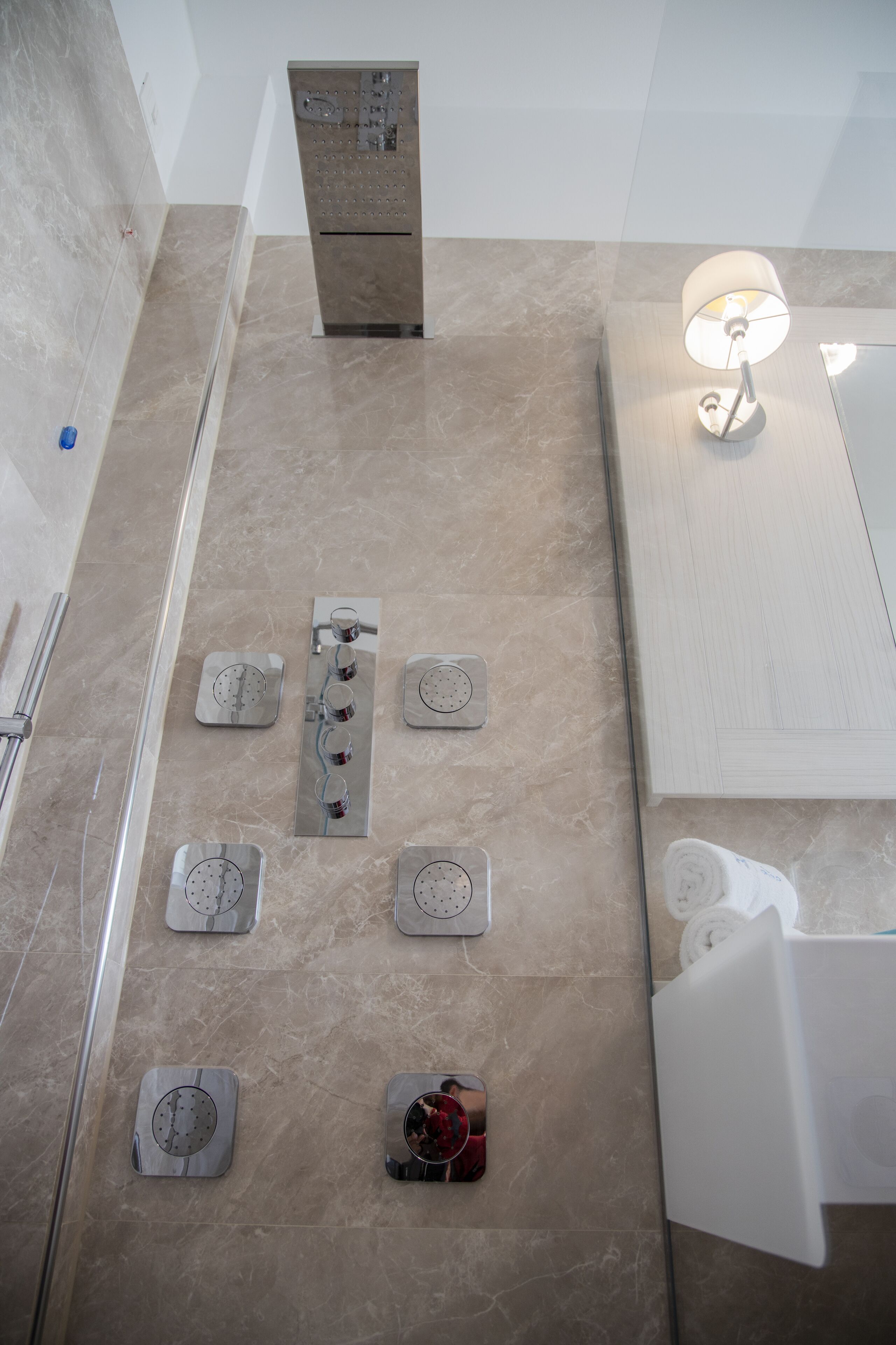 Een badkamer met een douche, meerdere kranen, een handdoekrek en een spiegel.