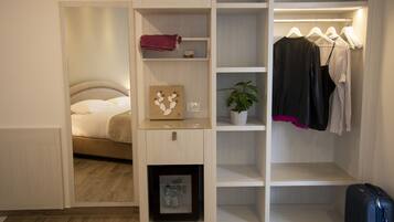 Una habitación de hotel con una cama, un armario, una planta pequeña y una maleta.