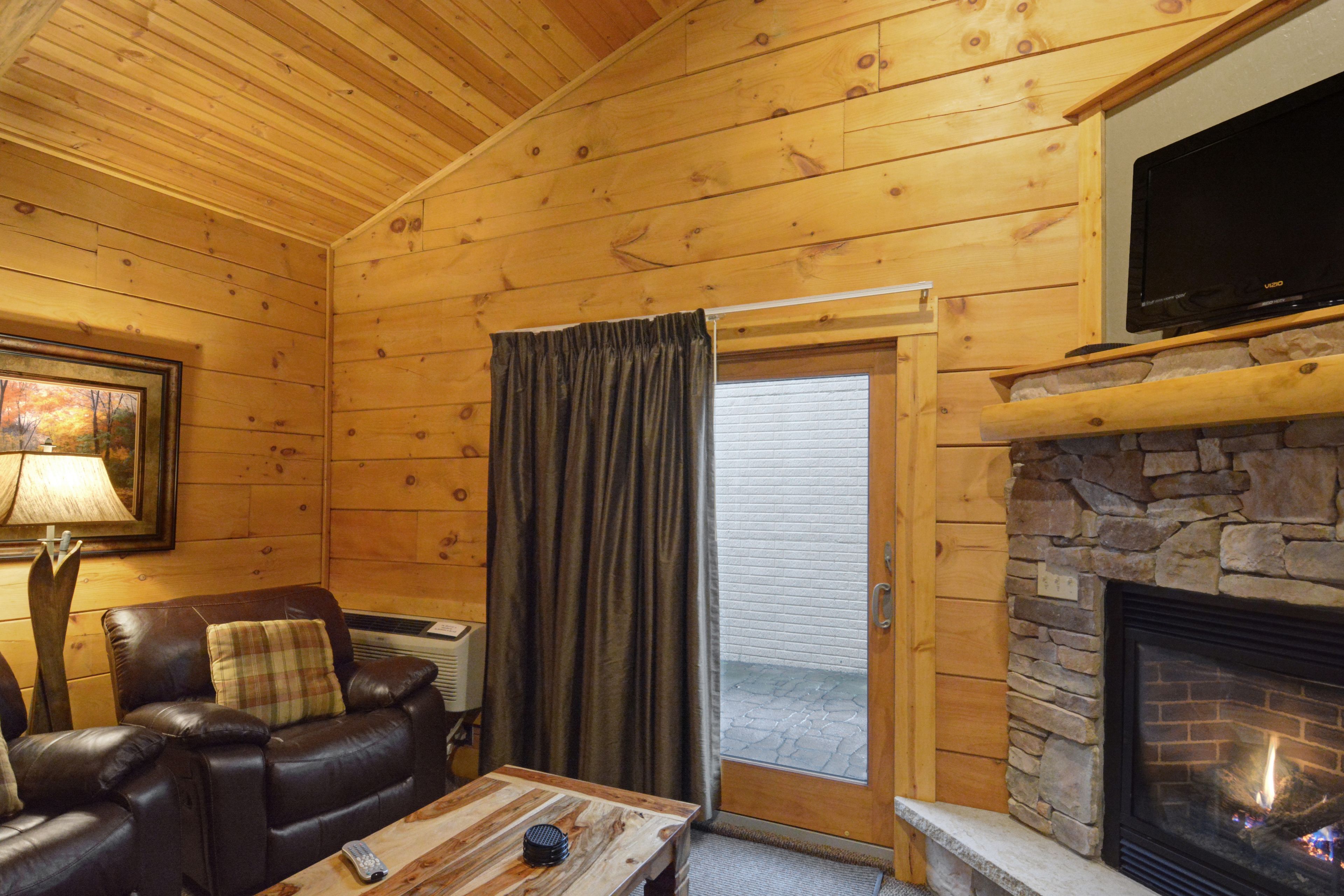 A cozy cabin interior with a stone fireplace, leather sofa, and a television mounted above it.