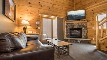 Een gezellig cabin interieur met een leren bank, een stenen openhaard, een televisie erboven en een houten plafond.
