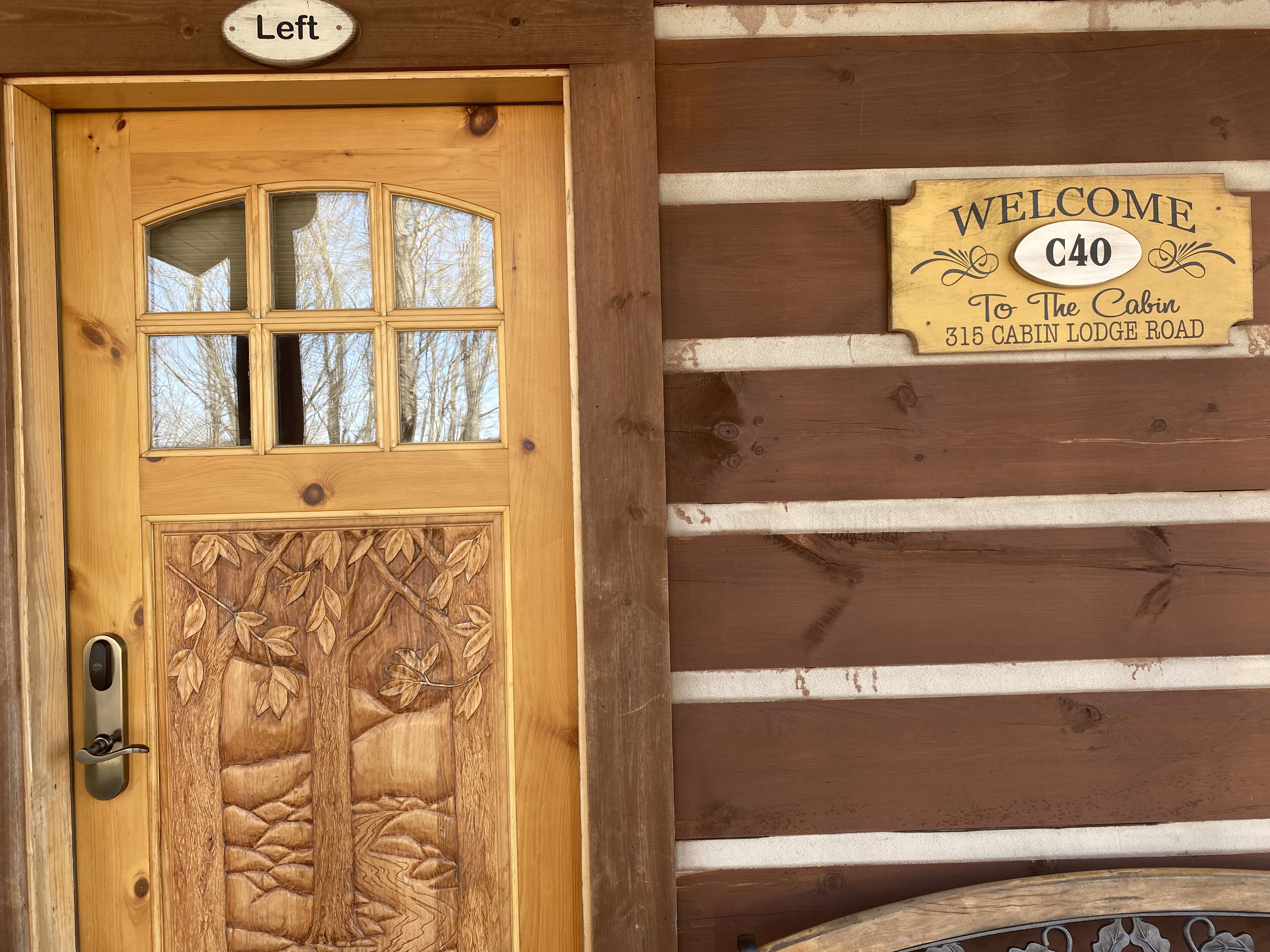 A wooden cabin door with a carved tree design and a 'Welcome' sign above it.