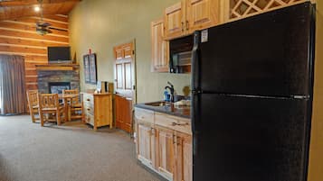 A kitchen with wooden cabinets, a black refrigerator, a stone fireplace, and a dining area with chairs and a table.