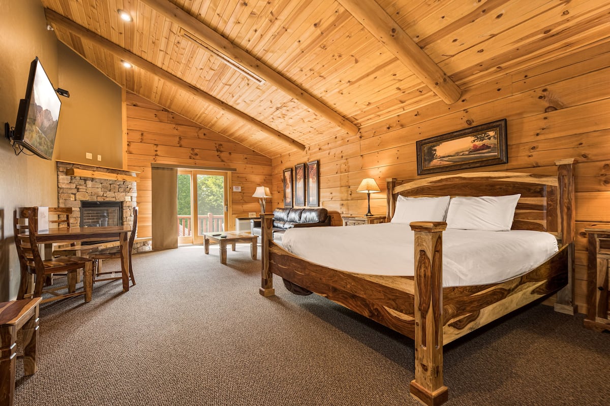 Ein schlafzimmer im Holzblockhaus-Stil mit einem großen Bett, einem Kamin aus Stein, einem Esstisch und einem an der Wand montierten Fernseher.