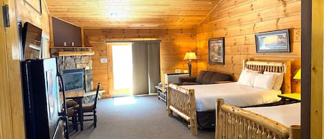 A log cabin room with a bed, a desk, a chair, a lamp, and a ceiling fan.