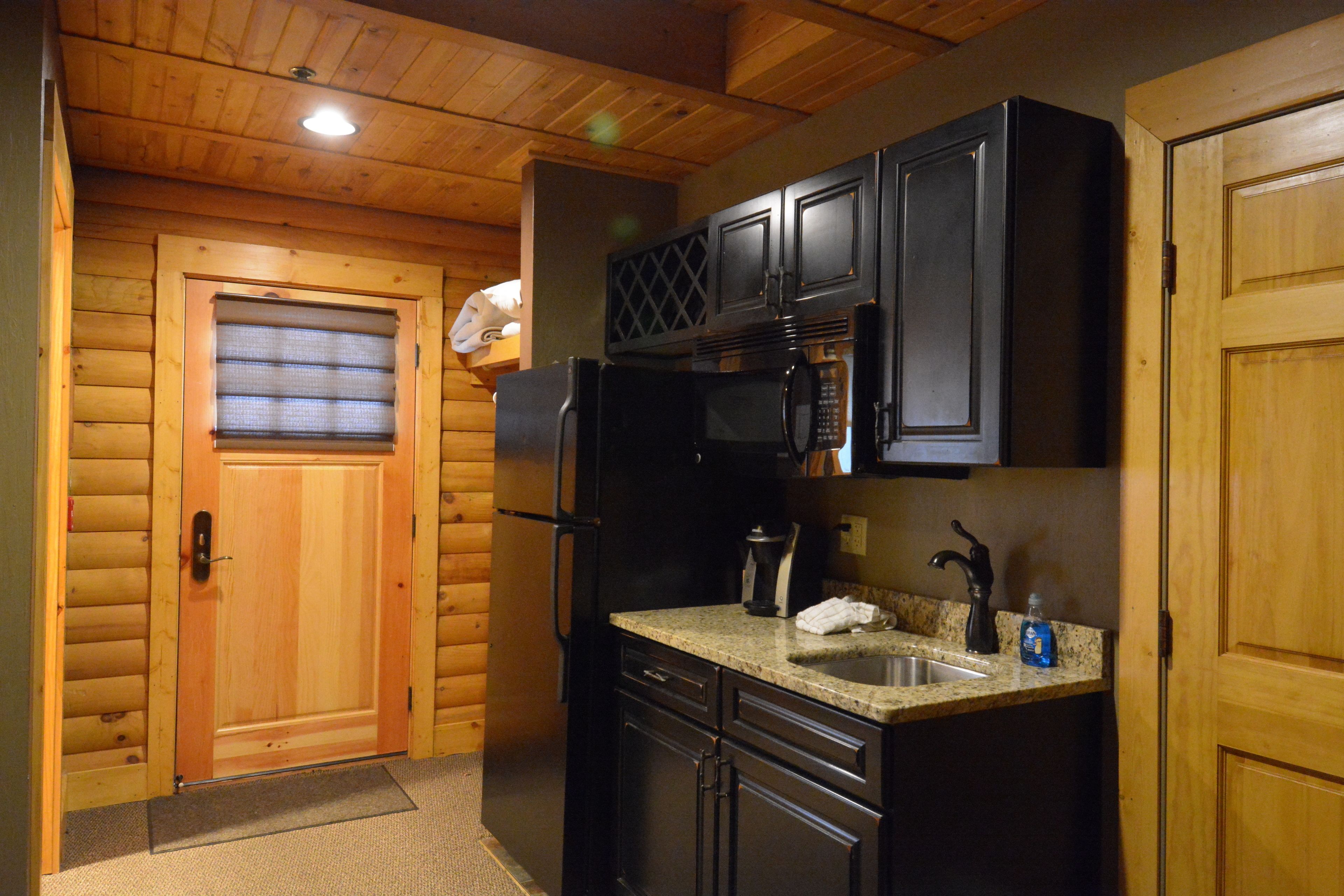 Una cocina compacta con muebles de madera, un refrigerador, un microondas y un lavamanos.