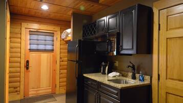 Una cocina compacta con muebles de madera, un refrigerador, un microondas y un lavamanos.
