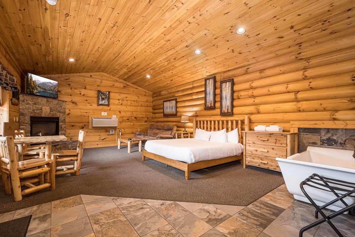 Ein Schlafzimmer in einer Blockhütte mit einem Bett, einem Schreibtisch, einem Sessel, einem Kamin, einem Fernseher und einer Badewanne.