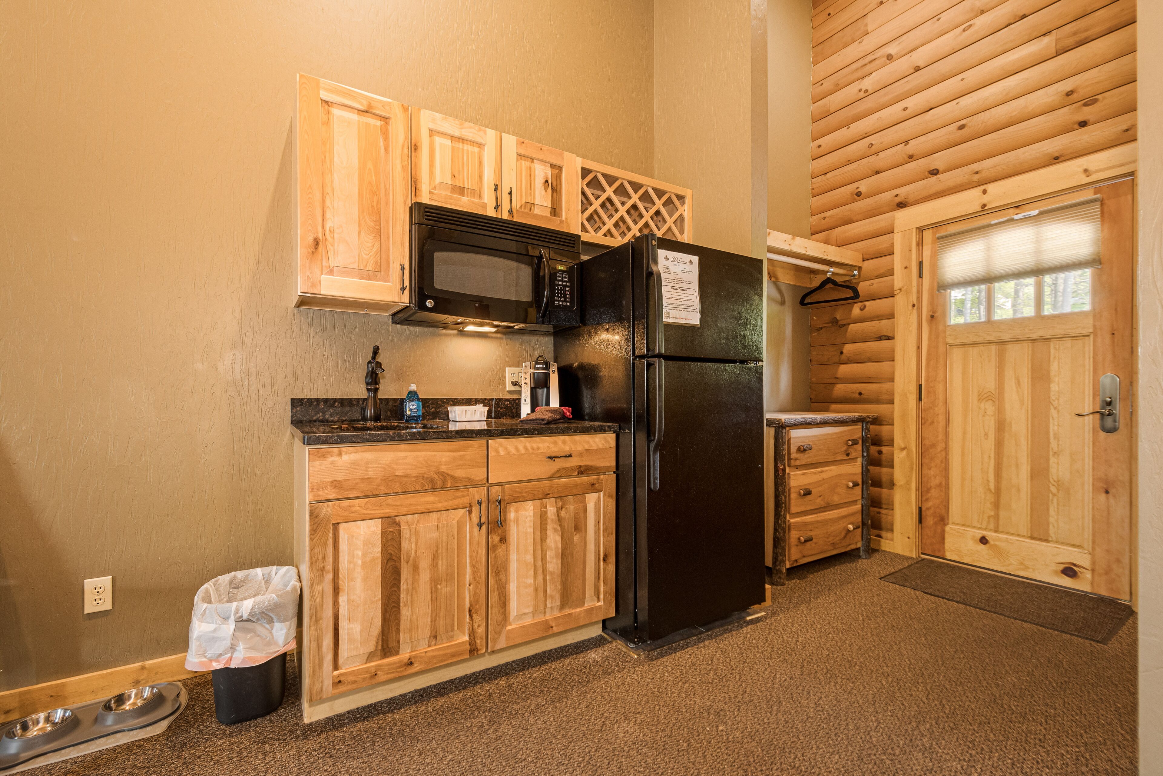 A compact kitchen with wooden cabinets, a black refrigerator, and a microwave.