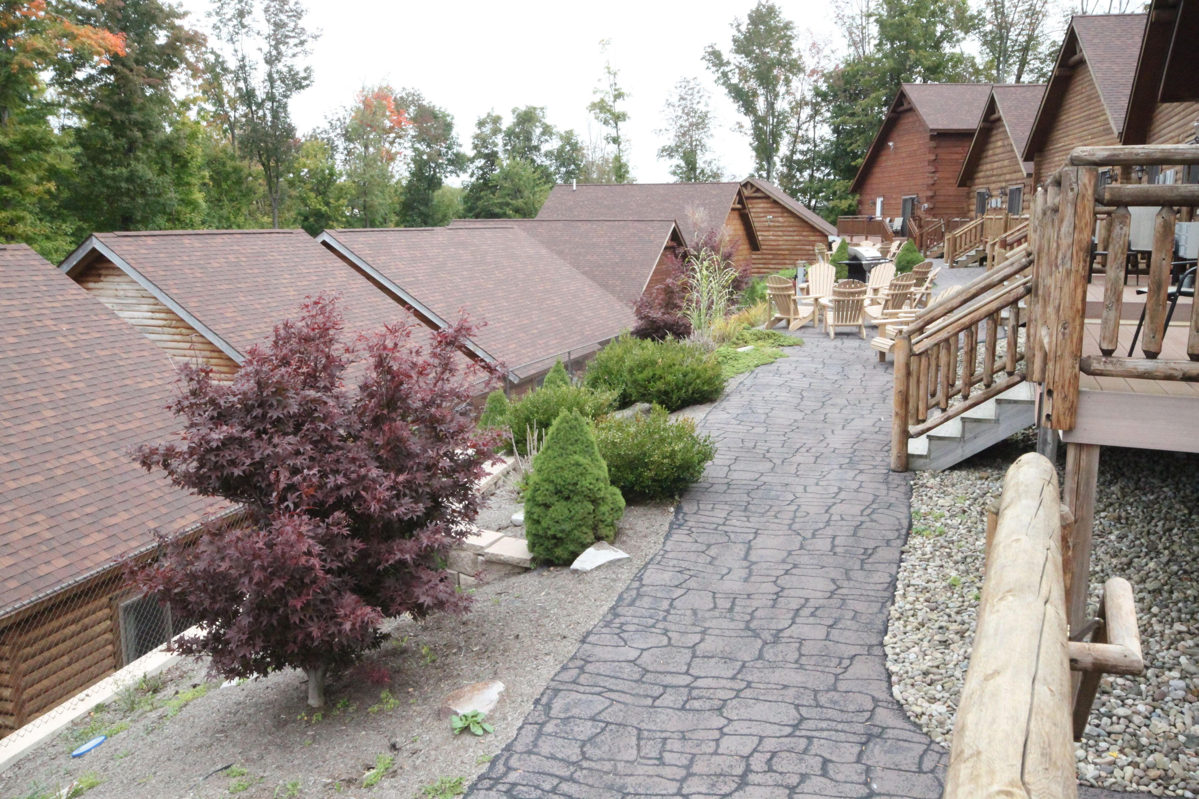 Une rangée de chalets en rondins, avec un sentier de pierres menant à une terrasse en bois.