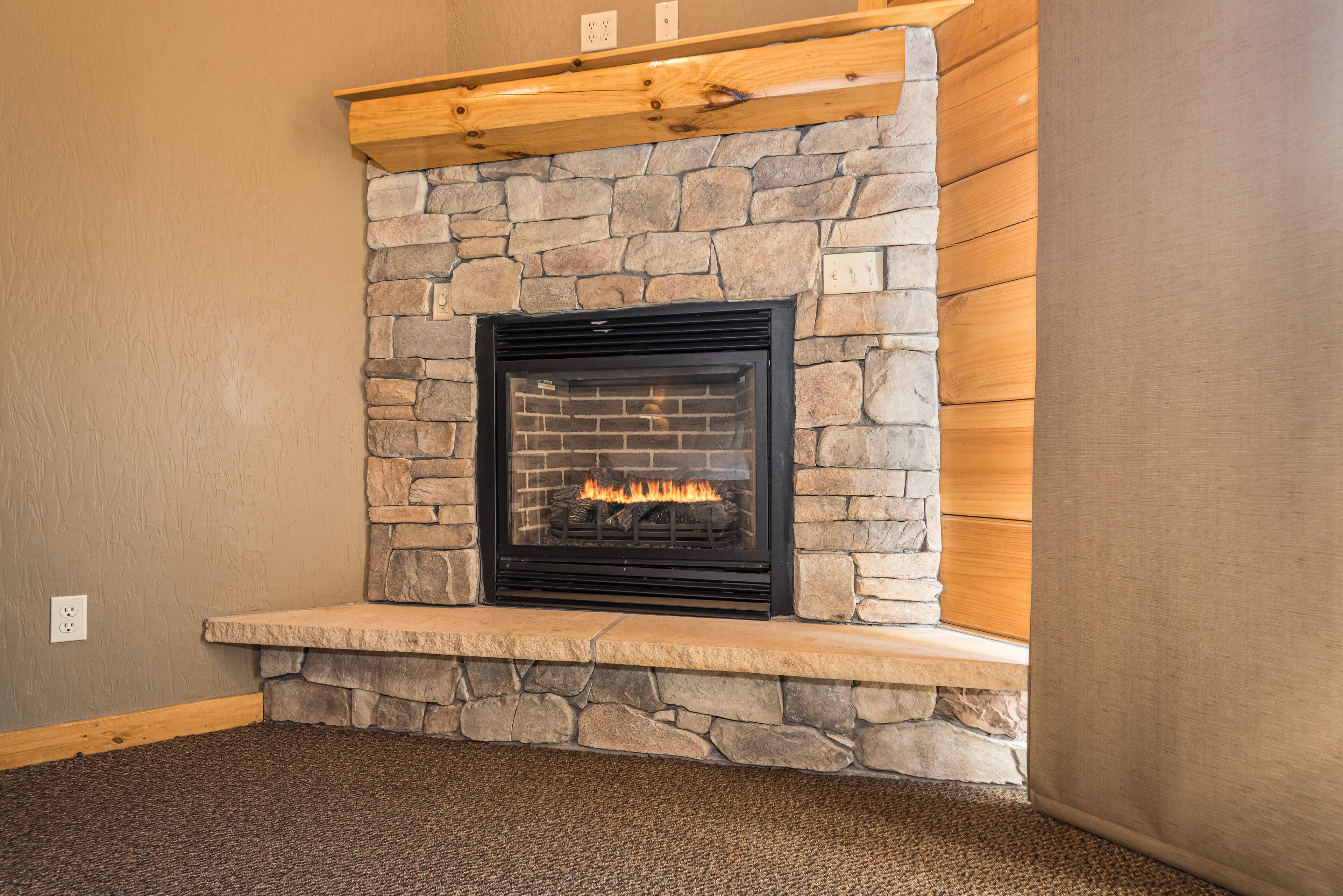 A stone fireplace with a black glass door, a wooden mantel above, and a stone base.