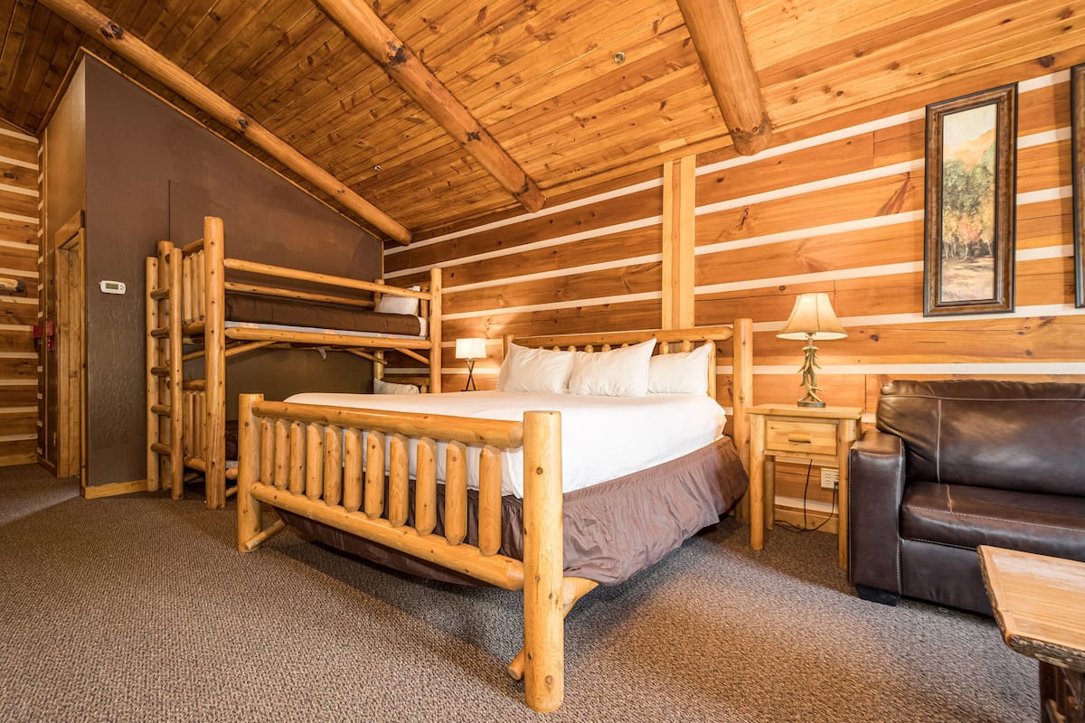 Ein Blockhauszimmer mit einem hölzernen Bett, einem Ledersofa, einem kleinen Tisch und einem Nachttisch.