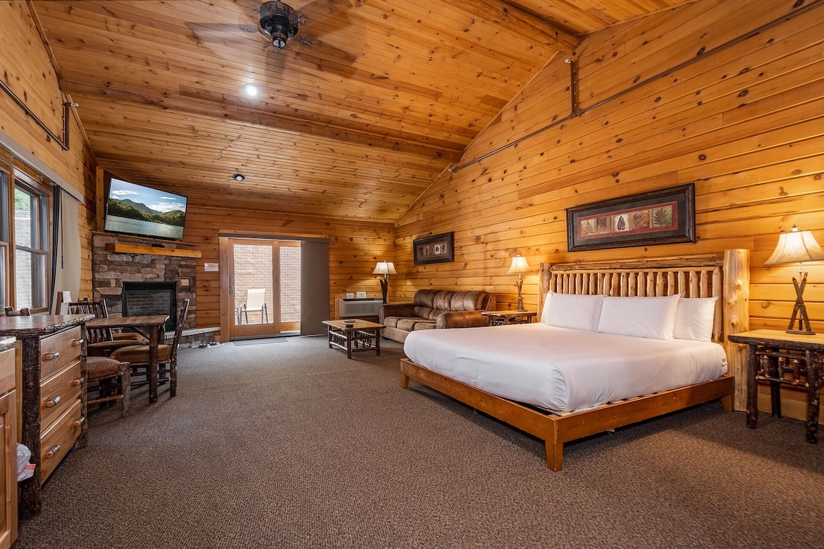 Ein Blockhauszimmer mit einem großen Bett, einem Kamin, einem Fernseher und einer Steinwand.