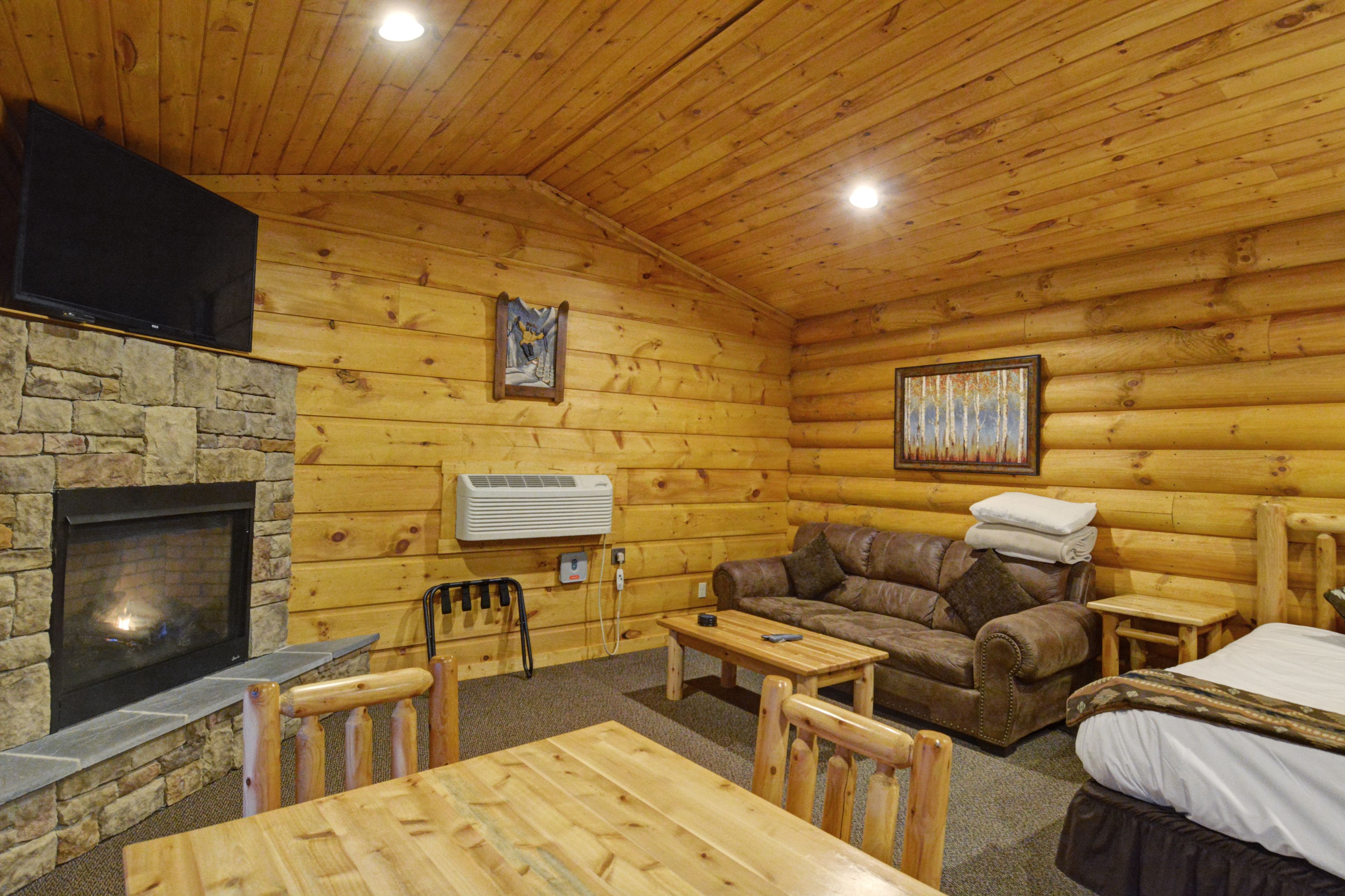 Interior de una cabaña de troncos con chimenea de piedra, muebles de madera, televisor y un cuadro en la pared.