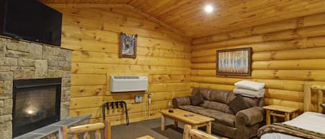 Ein Holzblockhaus-Interieur mit Kamin aus Stein, Holzmöbeln, einem Fernseher und einem gerahmten Bild an der Wand.