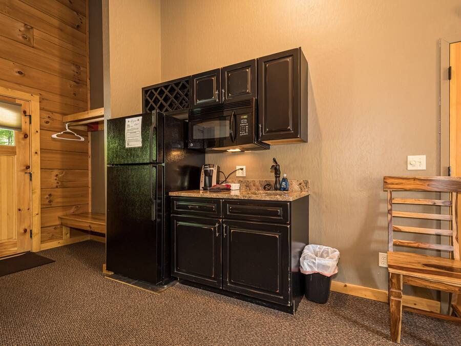 A compact kitchen with black cabinets, a microwave, and a refrigerator.
