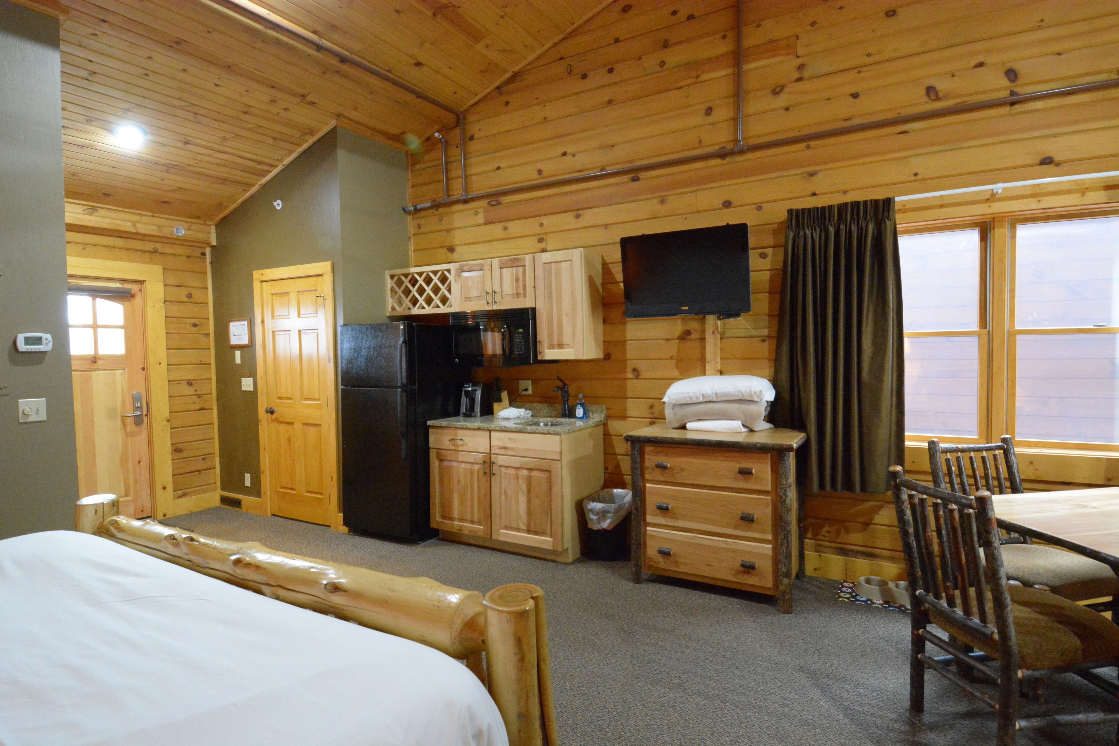 A wooden cabin with a bed, a dining table, a TV, and a kitchen area.