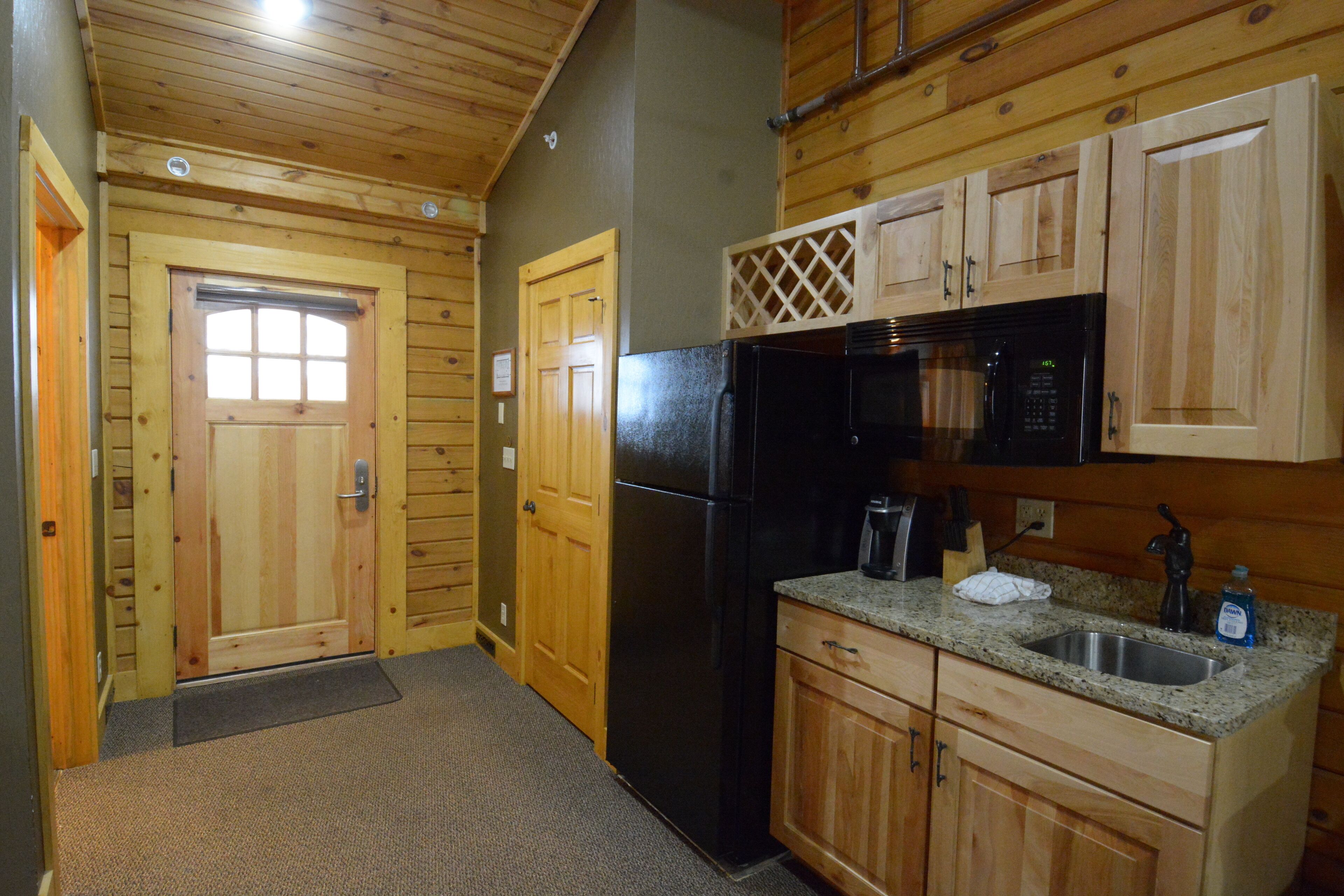 A compact kitchen with wooden cabinets, a black refrigerator, and a microwave.