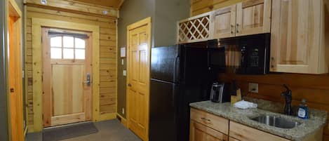 A compact kitchen with wooden cabinets, a black refrigerator, and a microwave.