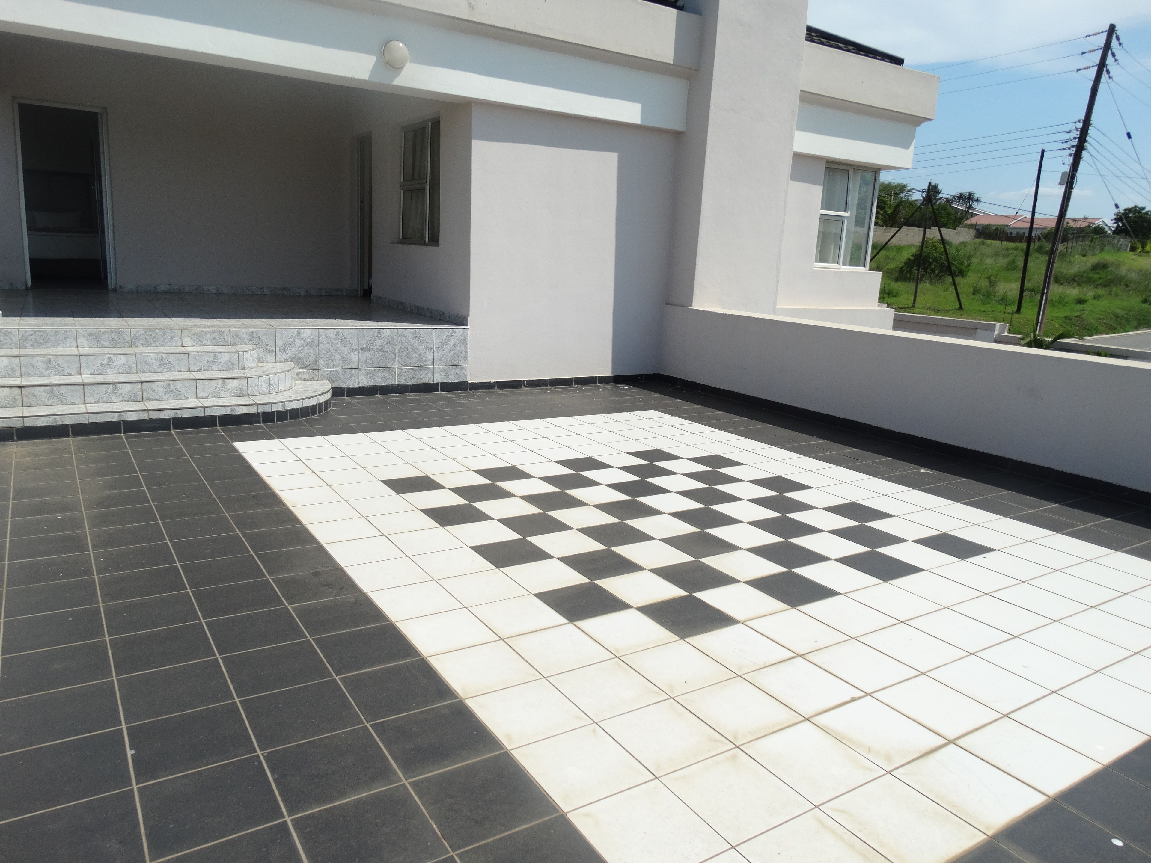 Un edificio moderno con un patrón de piso a cuadros, una escalera que lleva a una zona cubierta y vistas a un campo de césped.