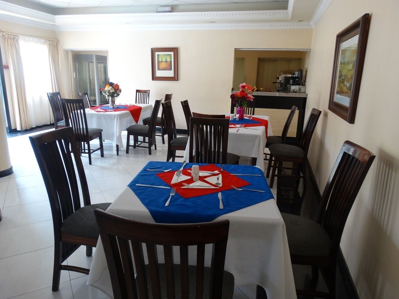 Comedor con mesas dispuestas para cuatro comensales, cada una con un camino de mesa rojo y azul.