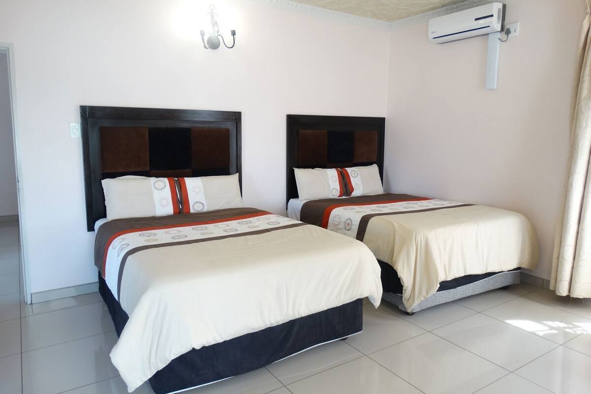 A hotel room with two beds, a ceiling light fixture, an air conditioning unit, and a curtain.