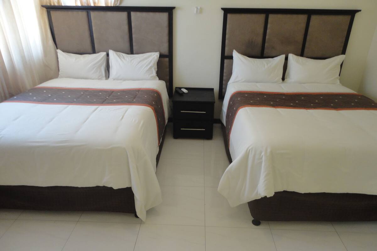 A hotel room with two single beds, each with a headboard, a nightstand, and a drawer.