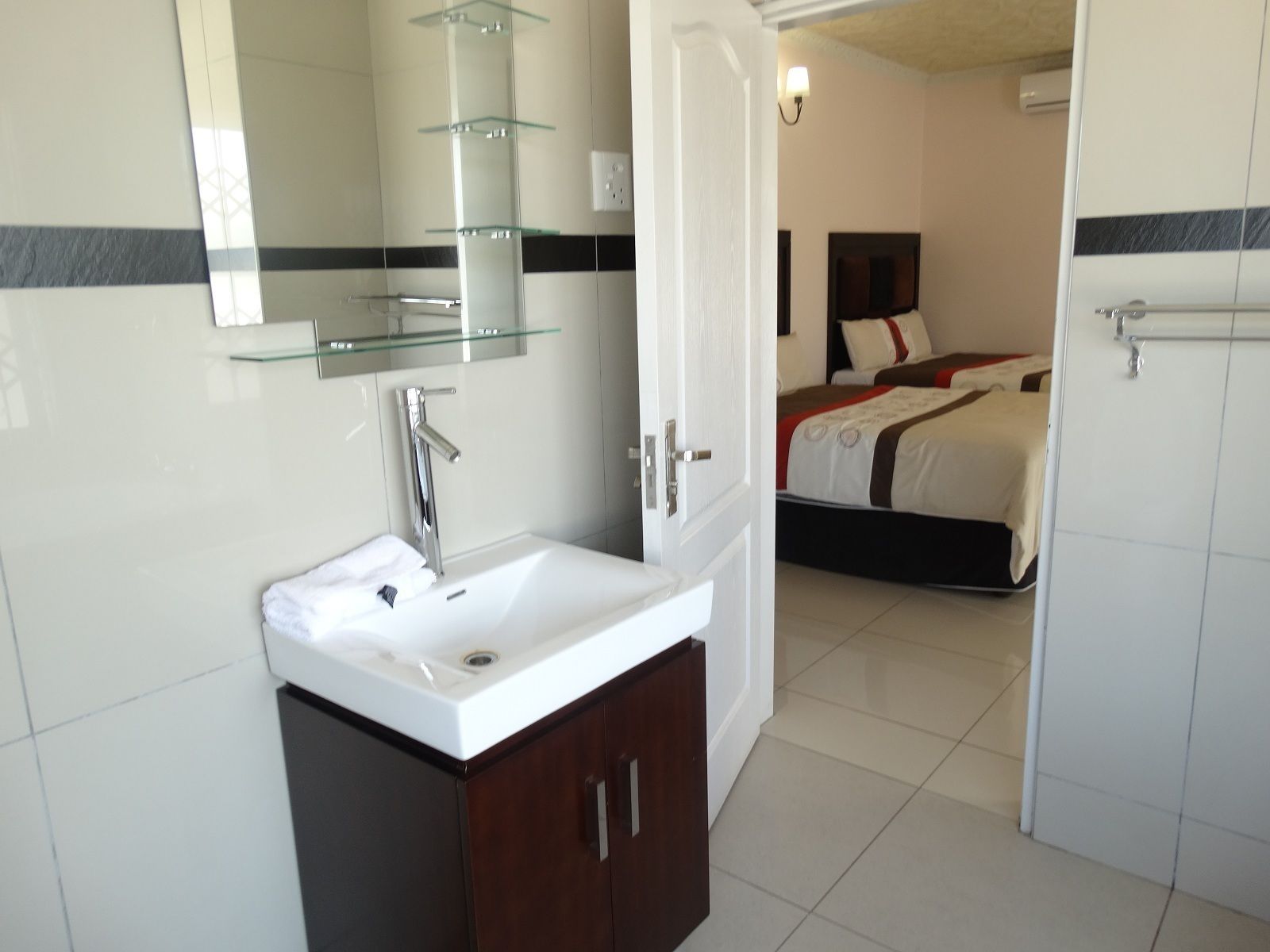 A hotel bathroom with a white sink, a glass shelf, and a mirror.
